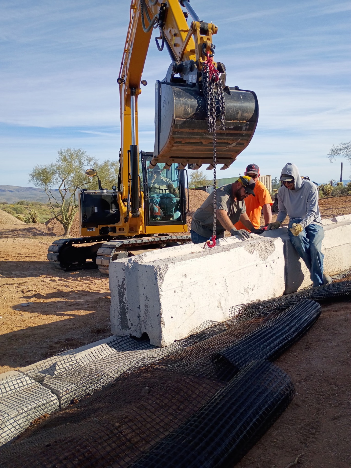 Crew setting a large concrete barrier block with the excavator
