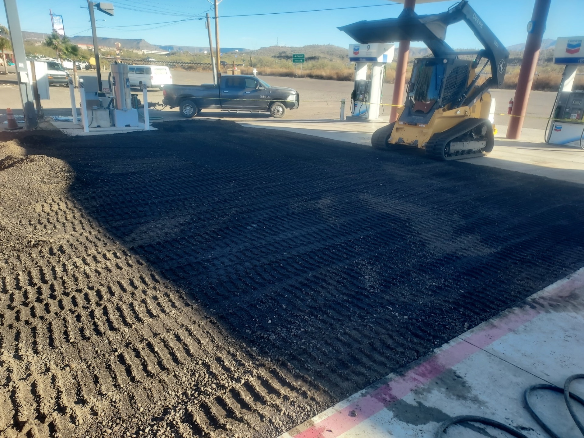 Deere skid steer laying fresh asphalt patch at a Chevron station