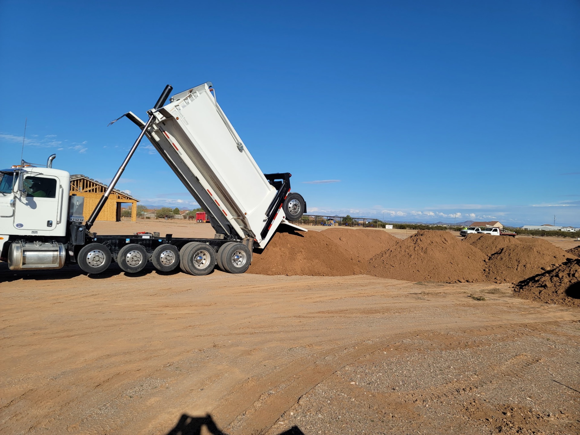 White Peterbilt end-dump tipping a load of fill on a new homesite