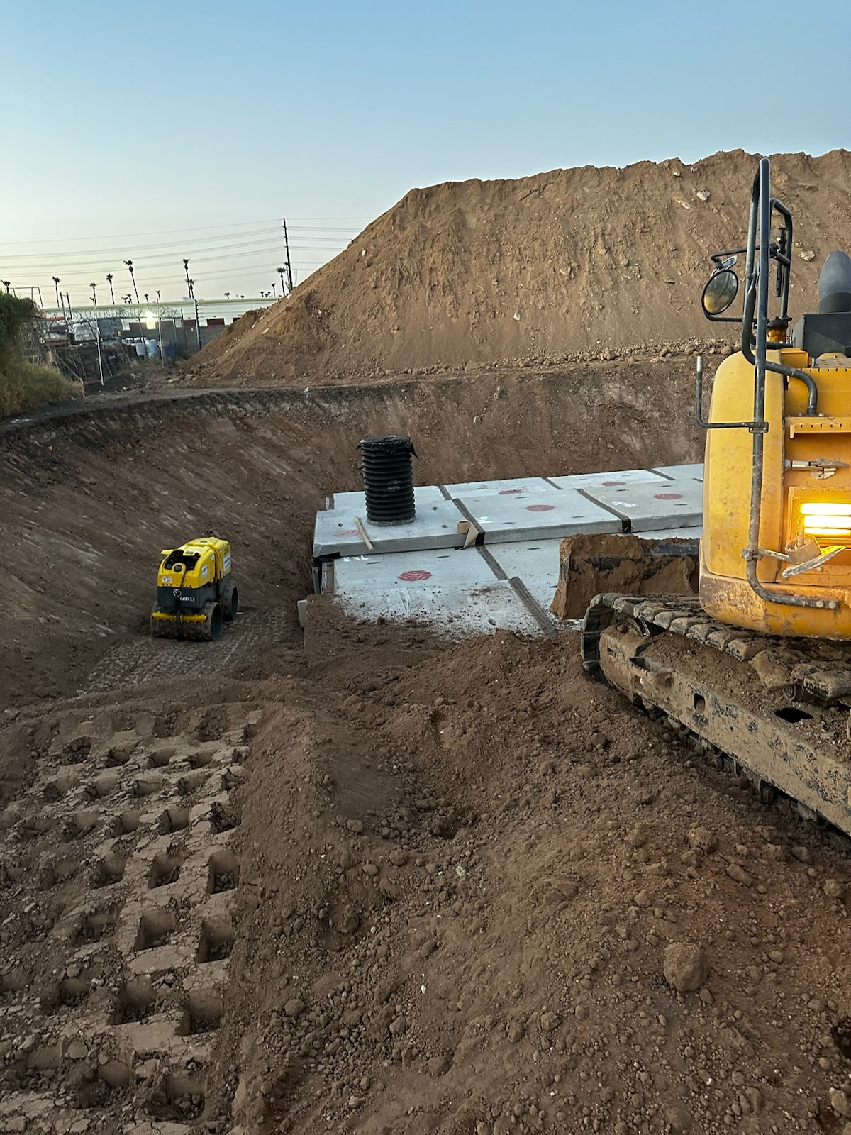 Compactor and mini-excavator at a wall install, sunset light
