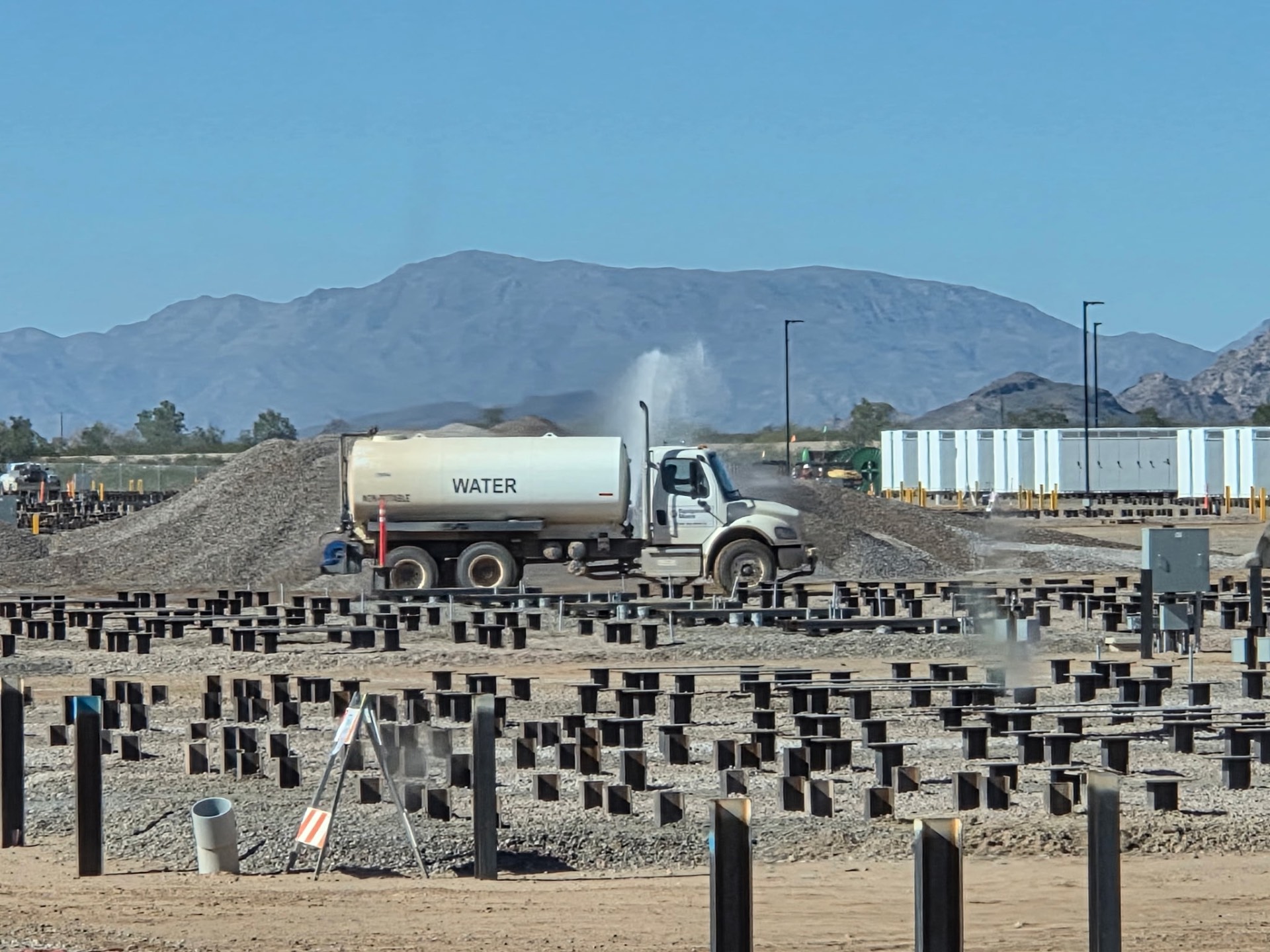 Water truck knocking down dust on a solar pile field with mountains behind
