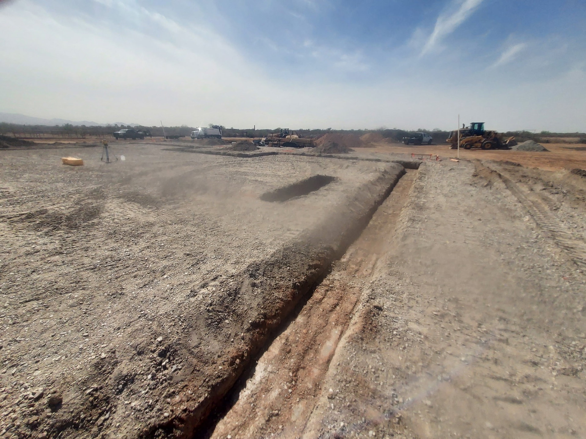 Wide site grading with fresh utility trench cut through a subdivision pad