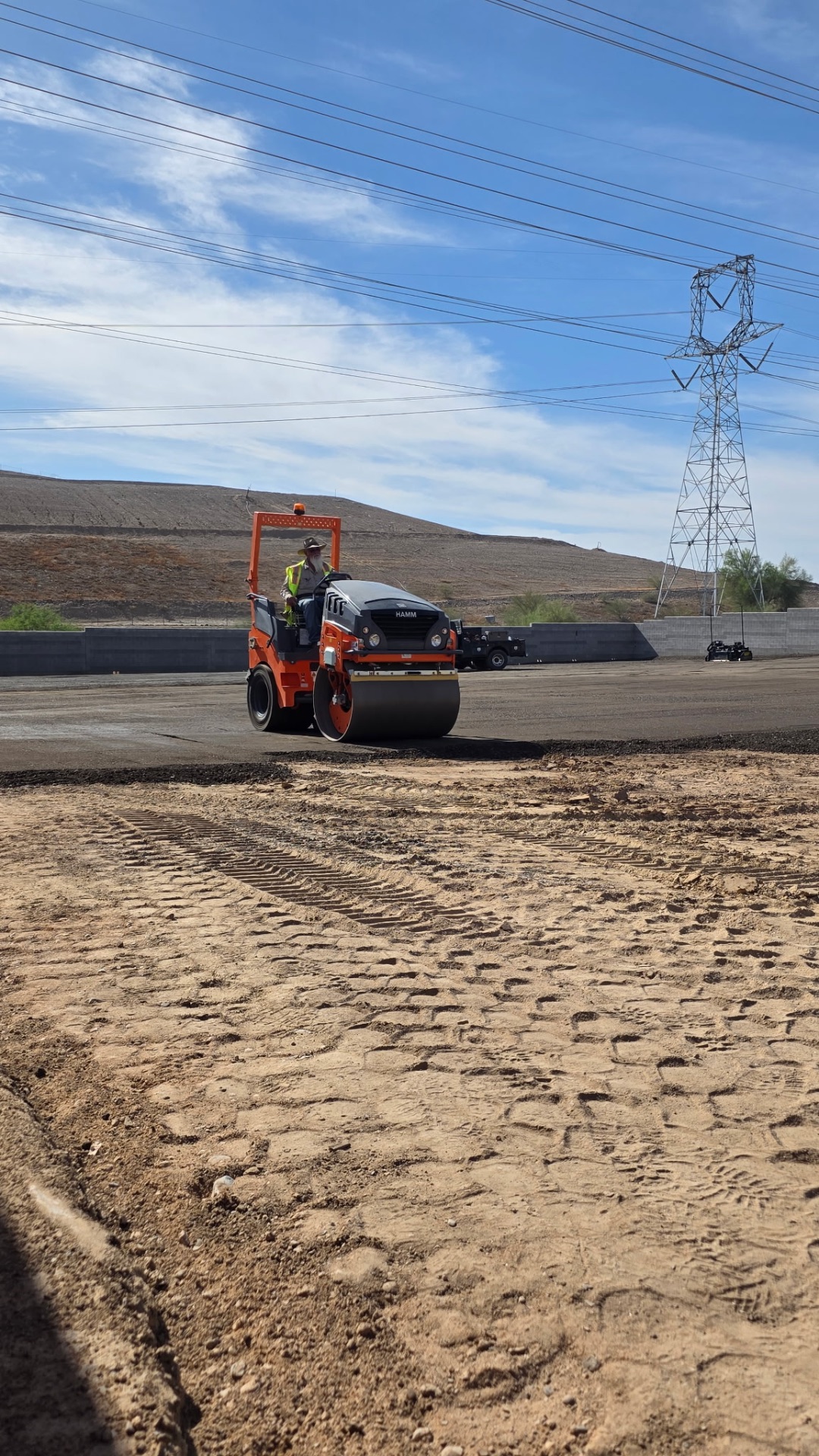 HAMM smooth-drum roller finishing a compacted pad under transmission lines